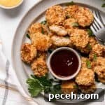 A plate of gluten free chicken nuggets with barbecue sauce and parsley for garnish.