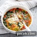Broth soup in white bowl with wilted greens, meatballs, and parmesan cheese.