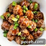Meatballs in sauce sprinkled with sesame seeds and green onions.