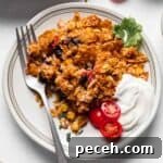 Chicken taco casserole on plate with sliced tomatoes and sour cream.