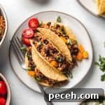 Three gluten-free ground chicken tacos on small plate with sliced cherry tomatoes and diced bell pepper.