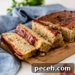 A chicken meatloaf on a wooden board with three slices cut.