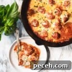 Meatballs in sauce and covered in cheese in large cast iron pan next to a serving on a white plate.