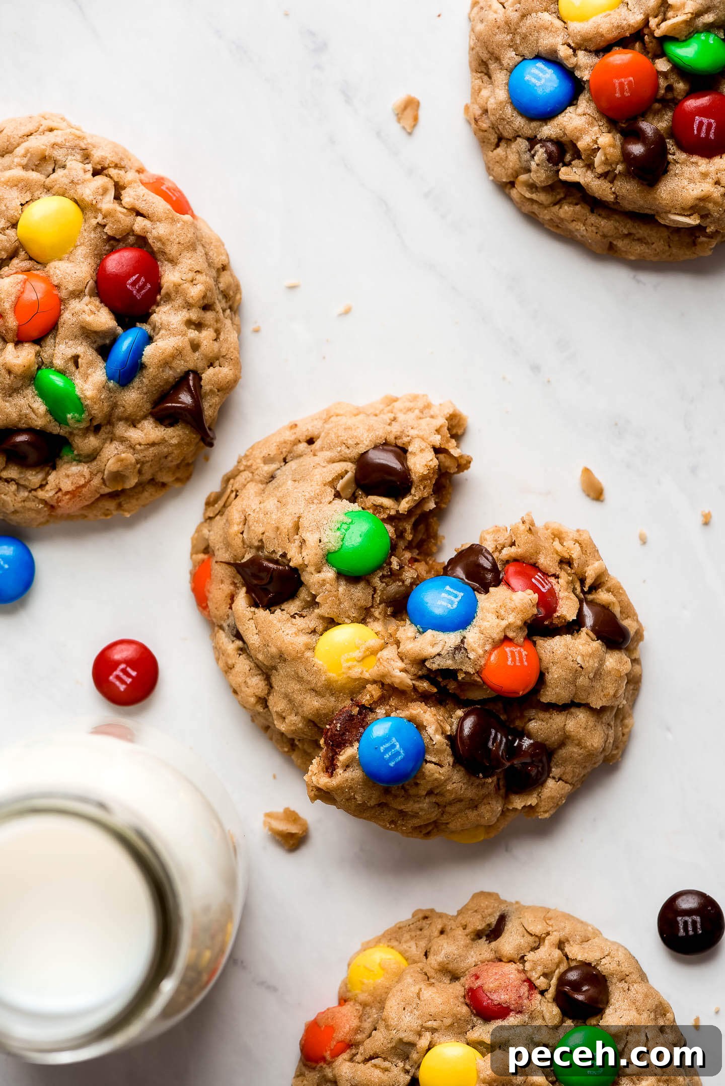 Soft Chewy Monster Cookies Recipe – Loaded Chocolate Chip Cookies 4 Peanut butter oatmeal cookies with chocolate chips and M&M's pressed into the top and a glass of milk to the side.