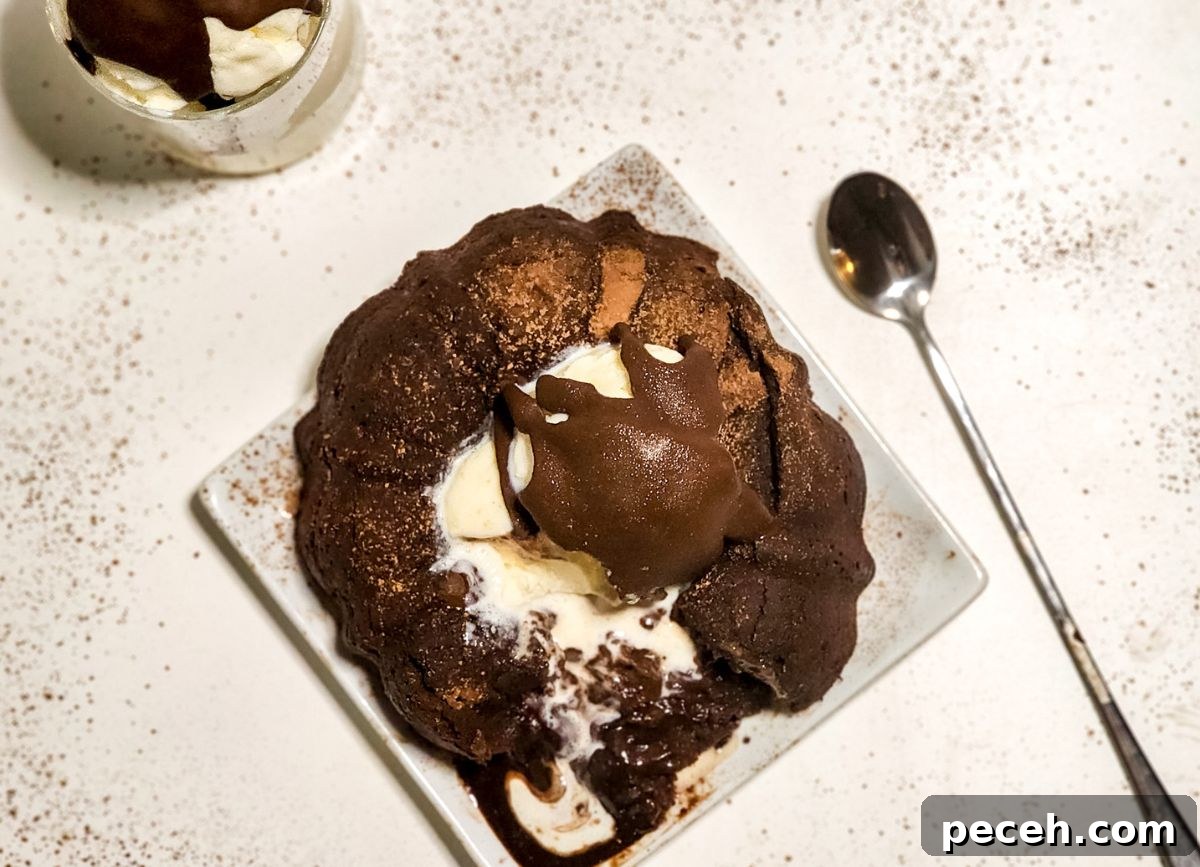 A chocolate molten lava cake broken open on a plate with a spoon next to it.