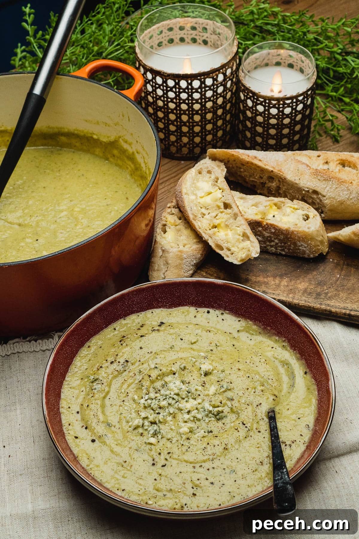 A bowl of blue cheese and broccoli soup and crusty bread and a cooking pot full with soup in the background