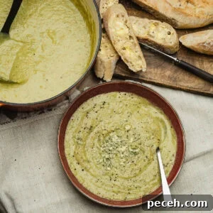 Broccoli and Stilton Soup Recipe in a bowl with stilton crumbled on top with slices of crusty bread on a board and a pot full with soup in the background