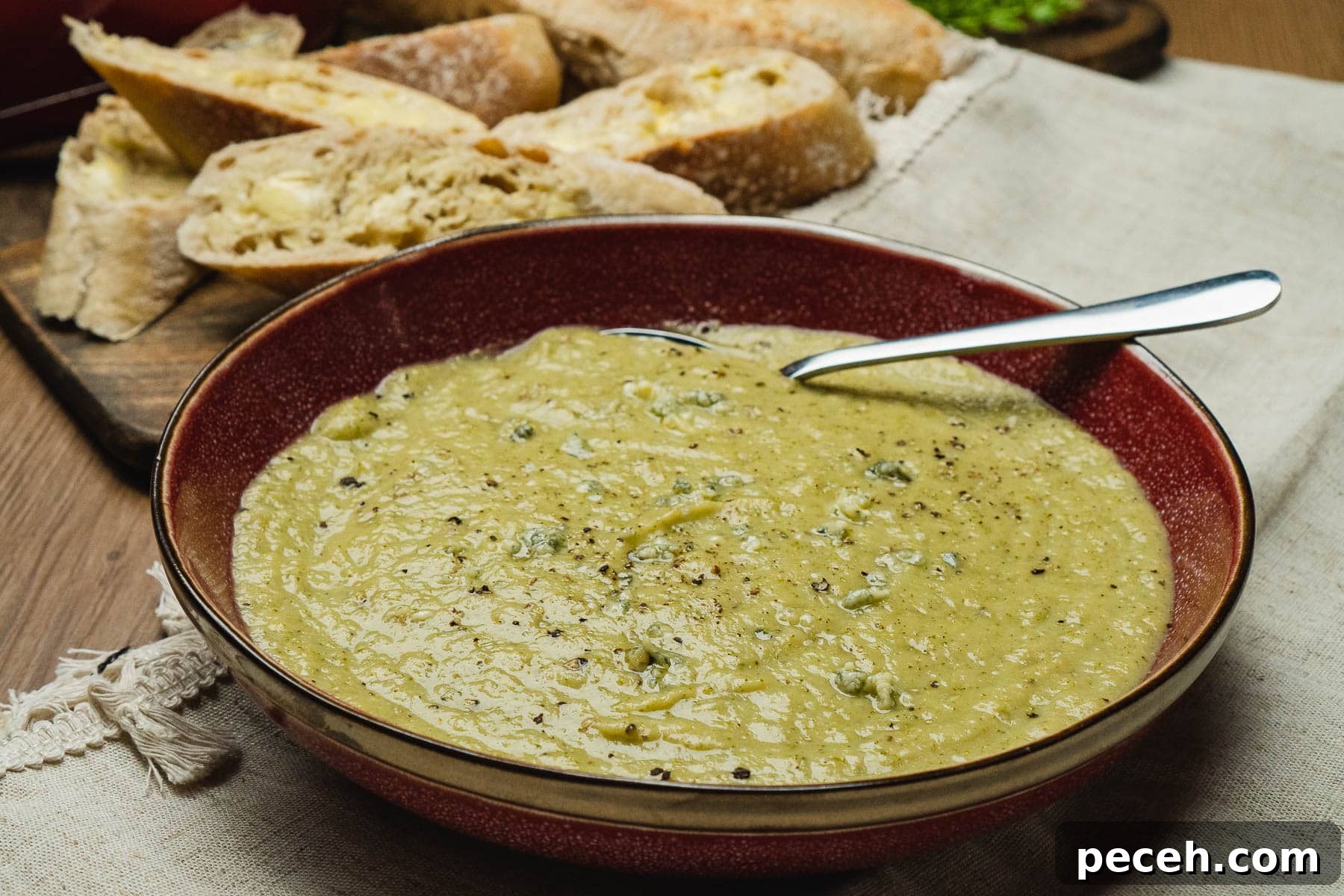 Broccoli and Stilton Soup Recipe in a red bowl with crusty bread in the background