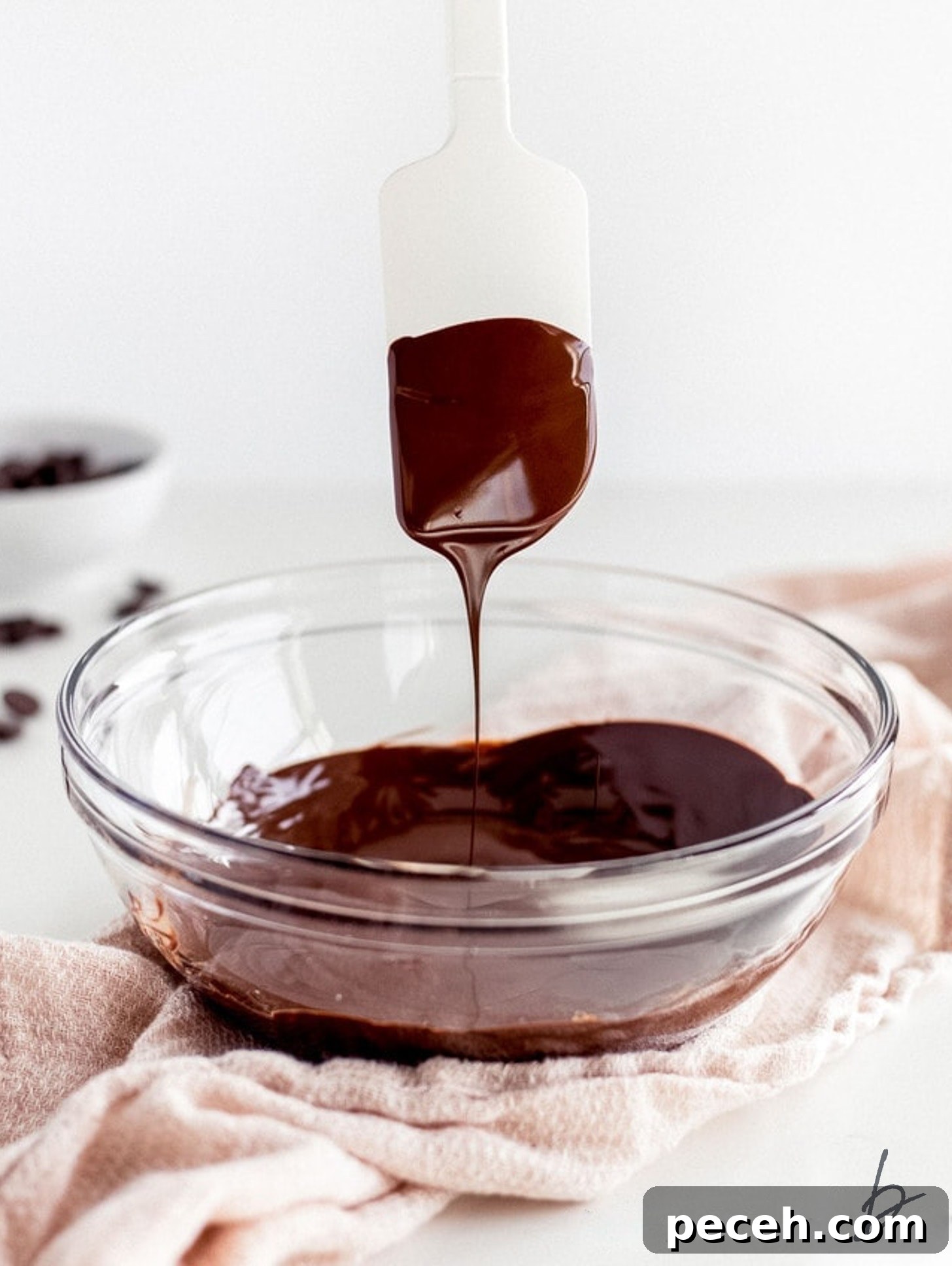 How to Melt Chocolate: Microwave and Stovetop Methods 2 silicone spatula with melted chocolate dripping into bowl of melted chocolate.