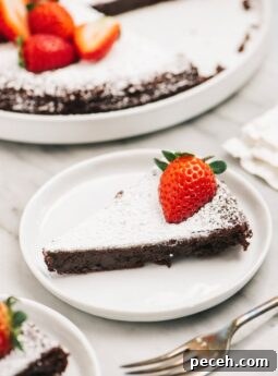 slice of flourless chocolate cake with powdered sugar and strawberry on white round plate
