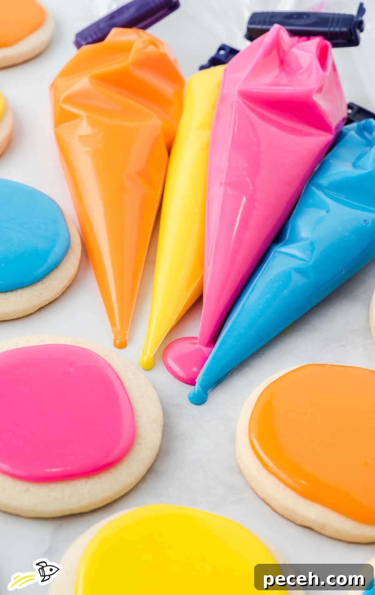 Simple Sugar Cookie Icing Recipe for Perfect Decorating 7 yellow, pink, blue, and orange icing in piping bags and also on top of sugar cookies