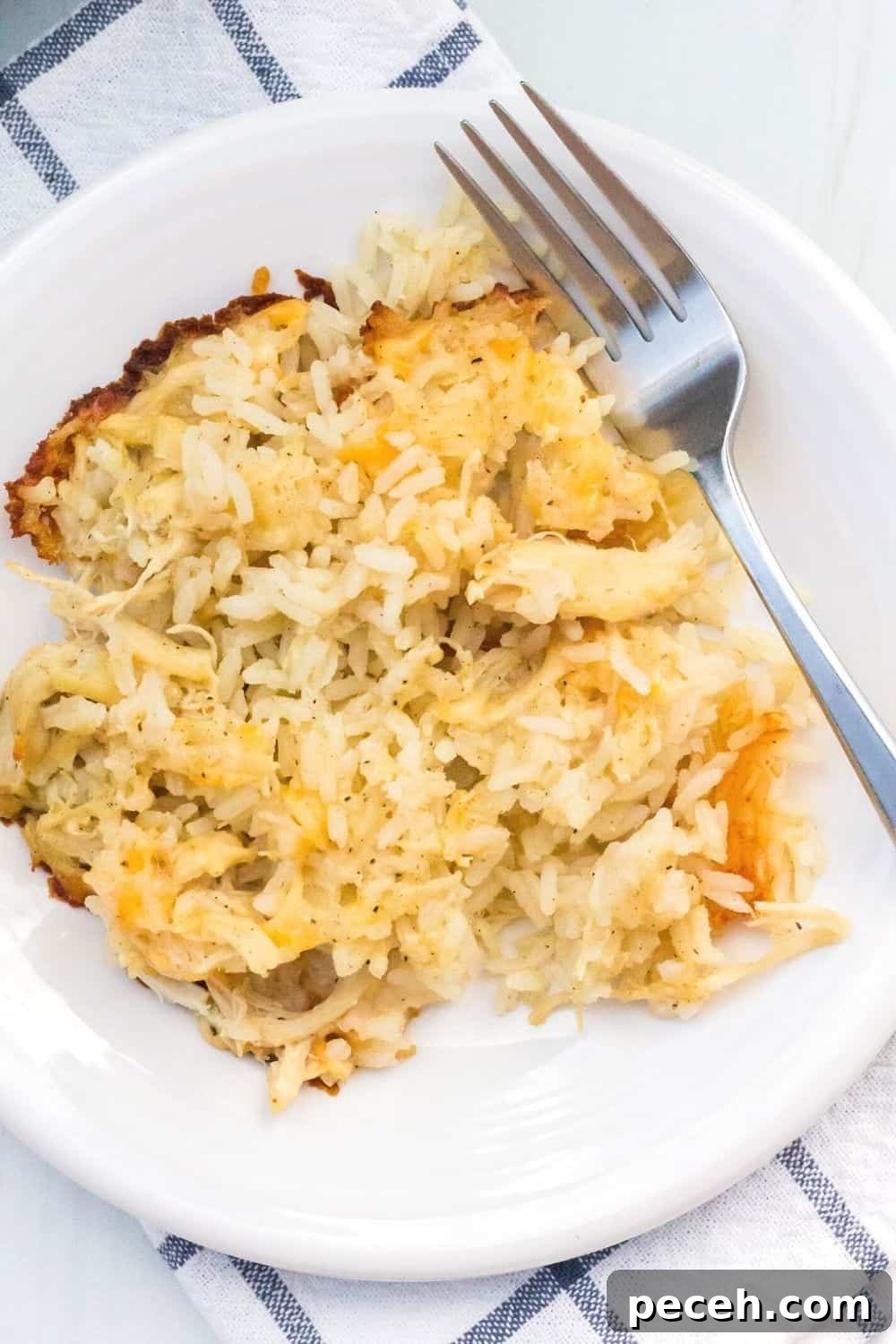 No-Peek Chicken and Rice Casserole: Tender, Foolproof Meal 3 overhead view of a white plate serving chicken and rice, with cheese interspersed and crispy cheese around the edges.