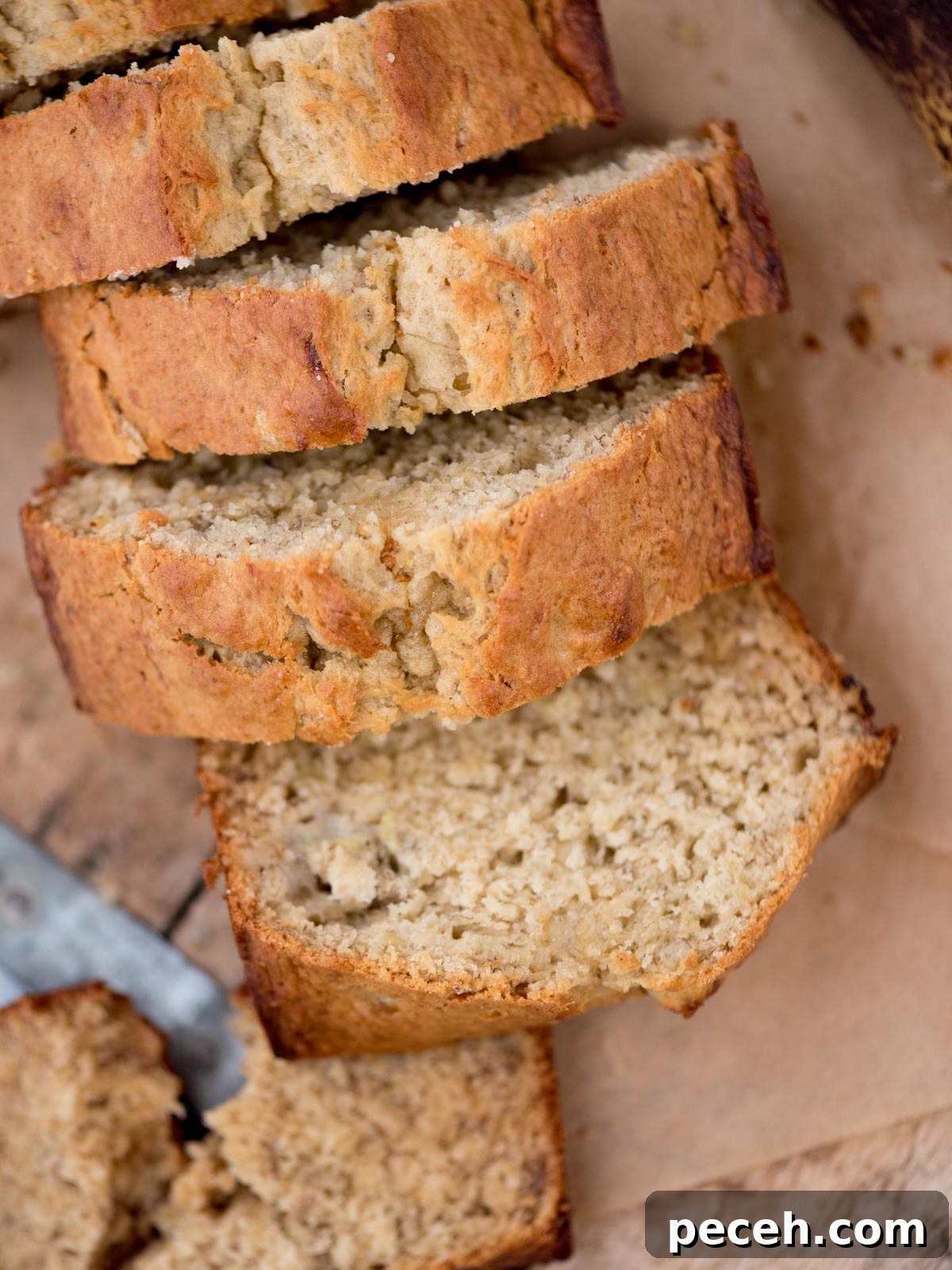 Classic Old-Fashioned Banana Bread Recipe for Perfect Loaf 2 Sliced banana bread on a wooden surface, showing a moist and dense texture. The golden-brown crust suggests its freshly baked. A knife is partially visible at the edge.