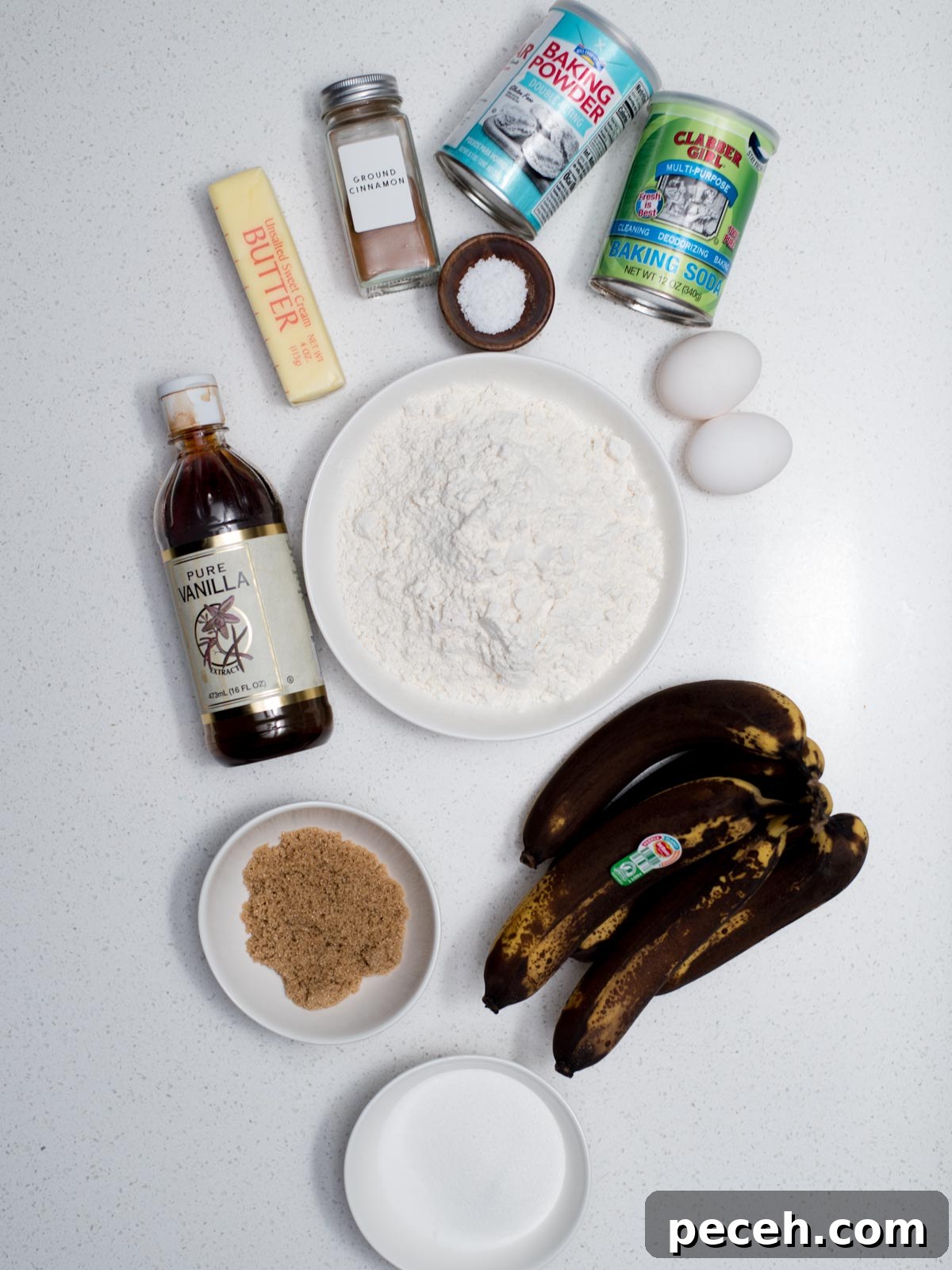 Classic Old-Fashioned Banana Bread Recipe for Perfect Loaf 3 Ingredients for baking on a white surface: brown bananas, flour in a bowl, eggs, a stick of butter, vanilla extract, brown sugar, baking powder, baking soda, cinnamon, and salt.