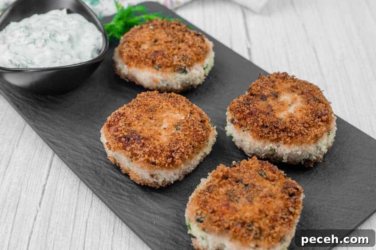 17 Mother’s Day Brunches You Can Enjoy Without Reservations or Parking Hassles 10 Four Salmon Cakes are arranged on a black slate serving board, accompanied by a small bowl of white sauce with herbs.