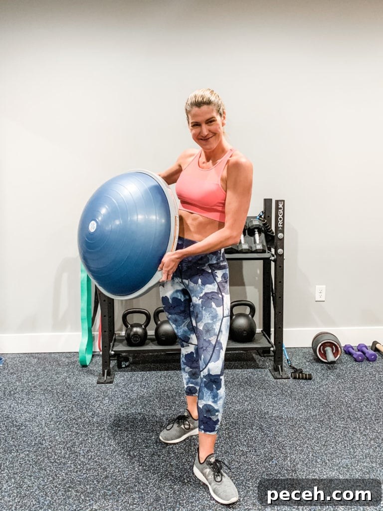 BOSU Ball Chest, Core & Quad Workout for Strength and Stability 2 A woman in floral leggings and a sports bra holding a bosu ball in a home gym