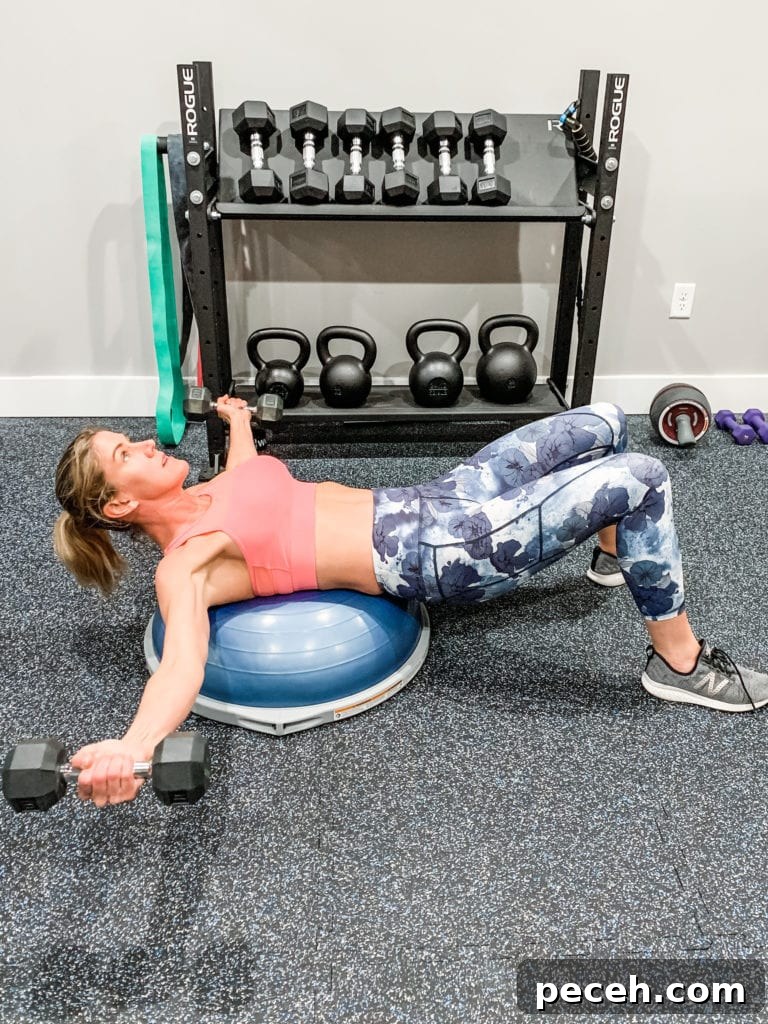 BOSU Ball Chest, Core & Quad Workout for Strength and Stability 4 a woman in floral leggings and a sports bra laying on a bosu ball and completing a chest fly exercise with dumbbells