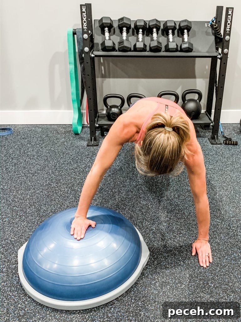 BOSU Ball Chest, Core & Quad Workout for Strength and Stability 7 A woman completing a push up with one hand on a Bosu Ball
