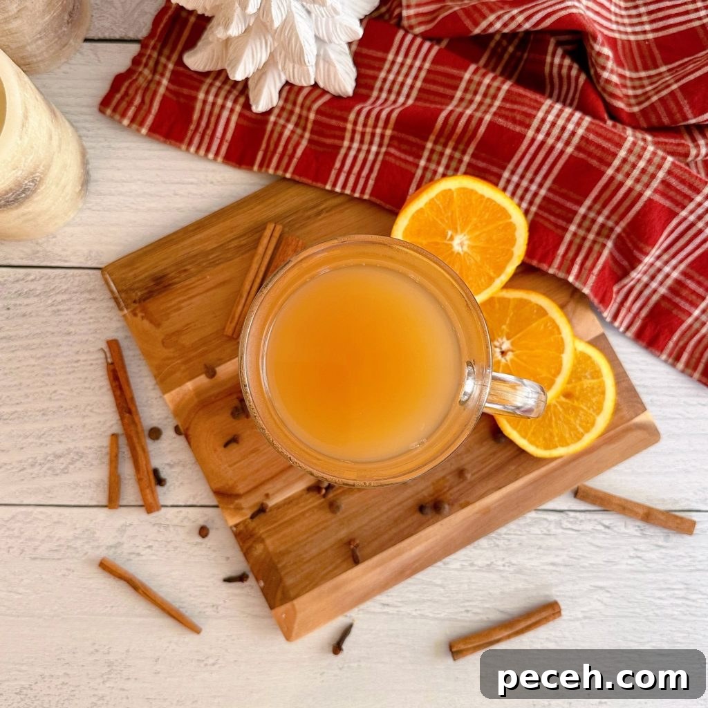 Spiced Cider in a mug on a board with spices and orange slices surrounding it.