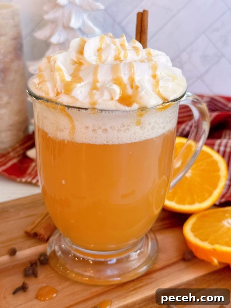 Close-up shot of Spiced Caramel Apple Hot Cider in a clear mug with whipped cream and caramel drizzle.