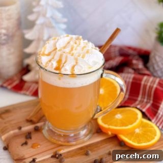 Glass of Old Fashioned Spiced Apple Cider on a cutting board with orange slices surrounding it. Topped with Whipped Cream and a caramel drizzle.