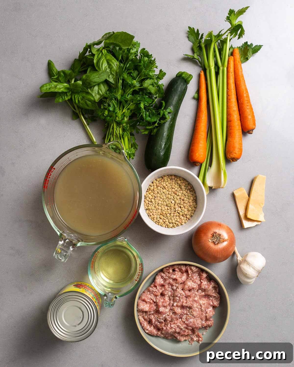 Hearty Sausage and Lentil Soup Recipe for Cozy Weeknights 3 Ingredients shown: herbs, zucchini, carrots, celery, chicken stock, lentils, onion, parmesan rinds, sausage, tomatoes, garlic, and dry whtie wine.