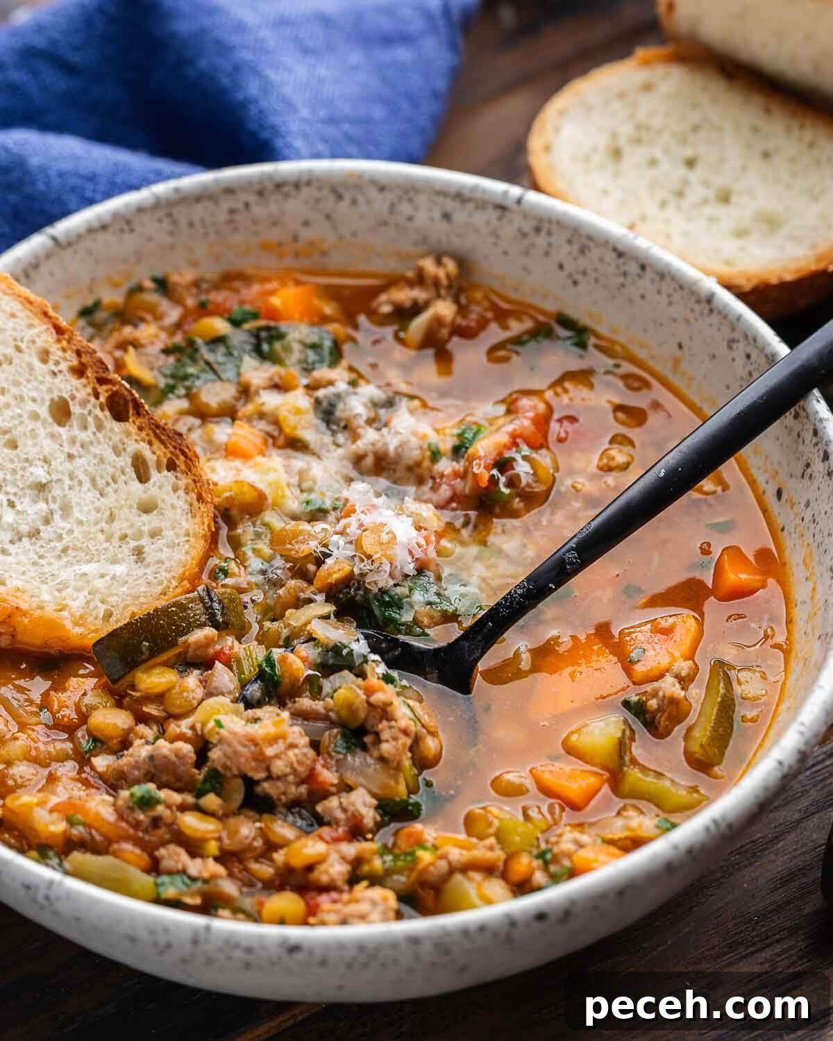 Hearty Sausage and Lentil Soup Recipe for Cozy Weeknights 5 Sausage lentil soup in white bowl with slice of bread and blue napkin in the background.