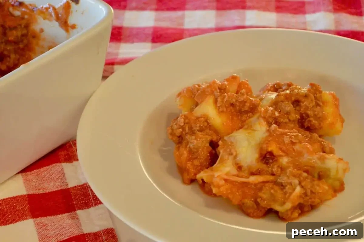 Cheesy Baked Tortellini Casserole with Rich Meat Sauce 3 Baked tortellini casserole serving in a white bowl on a checkered napkin.