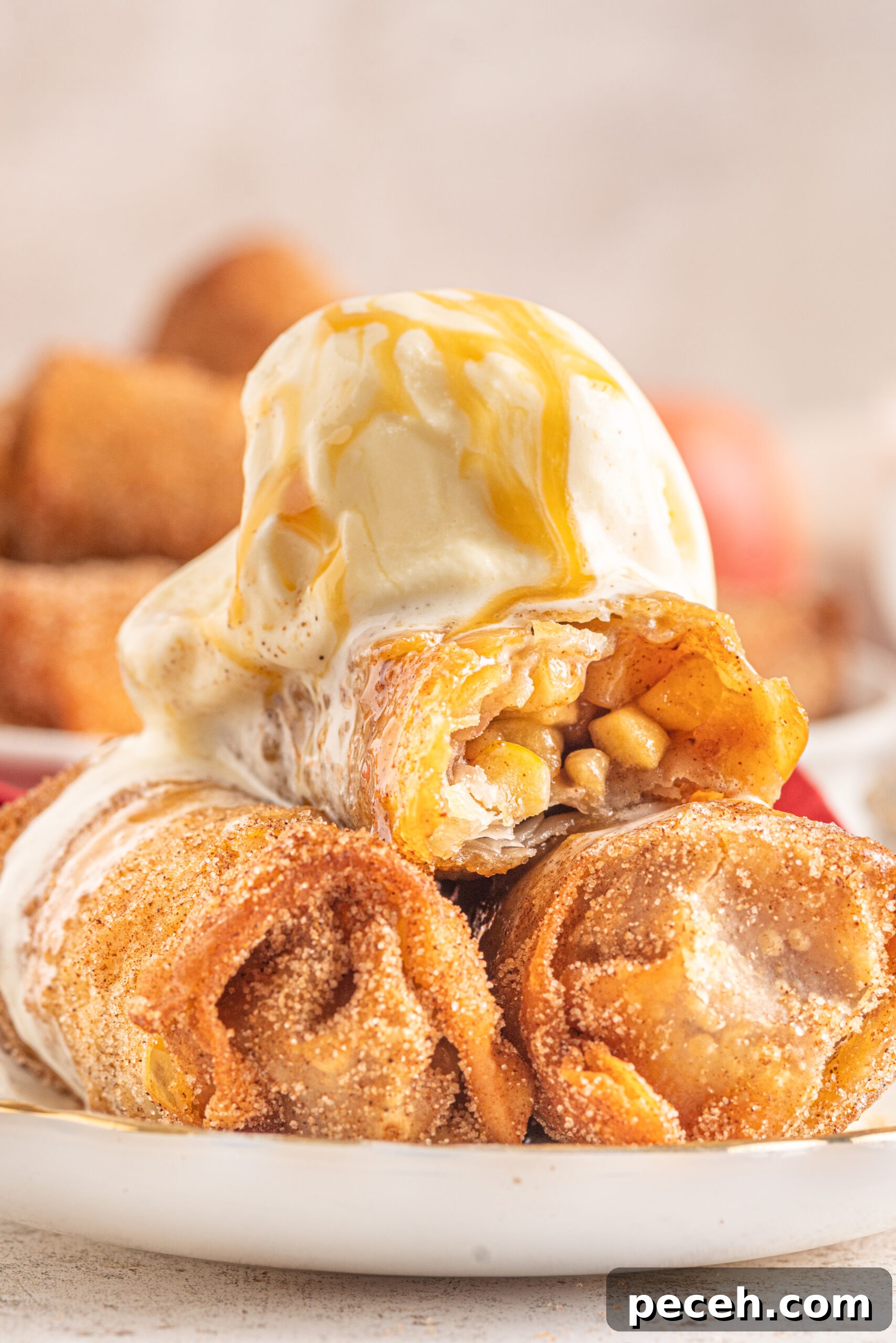 Crispy Apple Pie Egg Rolls with Cinnamon Sugar Dip 2 Three Apple Pie Egg Rolls stacked on a white plate with ice cream and caramel sauce on top.