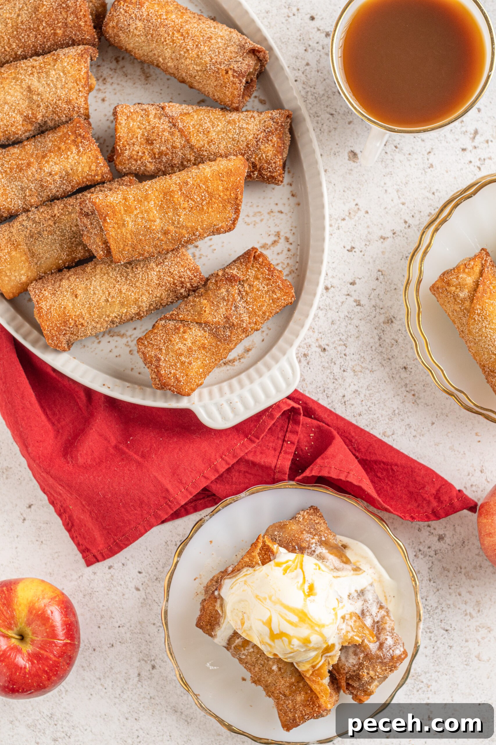 Crispy Apple Pie Egg Rolls with Cinnamon Sugar Dip 12 Overhead view of Apple pie egg rolls stacked on a white platter with apples and a red linen in the background.