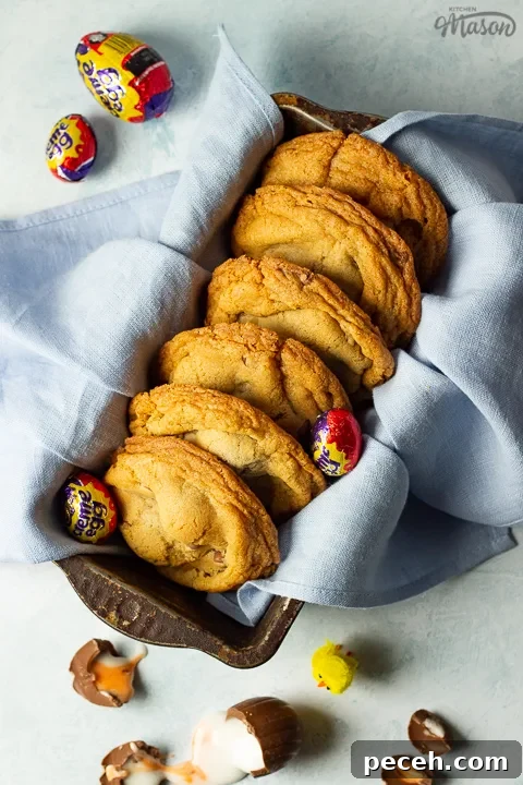 Crème Egg Cookie Recipe: Gooey Chocolate and Cadbury Filling 21 Birds eye view of Creme Egg cookies in a bread tin lined with a pale blue napkin surrounded by whole and broken Creme Eggs. Set on a pale blue backdrop with a yellow Easter chick in the background.