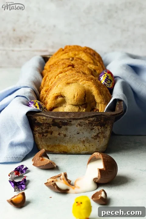 Crème Egg Cookie Recipe: Gooey Chocolate and Cadbury Filling 5 Front view of Creme Egg cookies in a bread tin lined with a pale blue napkin surrounded by whole and broken Creme Eggs. Set on a pale blue backdrop with a yellow Easter chick in the background.