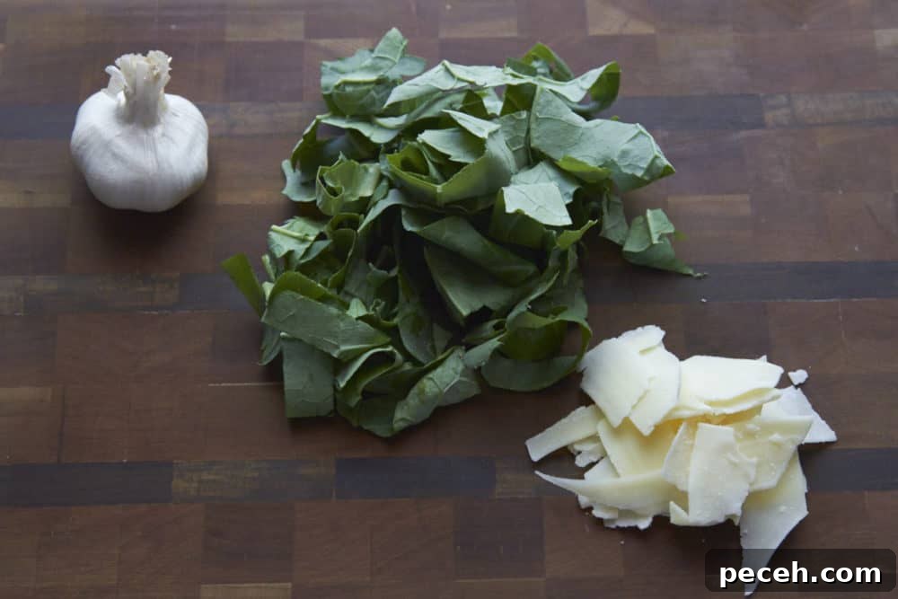 Kale and Walnut Pesto Recipe — Bright Sauce for Pasta & Toast 3 Fresh kale, a head of garlic, and shredded parmesan cheese on a wooden cutting board.