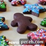 No-Chill Chocolate Cut-Out Sugar Cookies — Crispy, Ready Fast 9 an unfrosted chocolate sugar cookie among frosted chocolate sugar cookies on brown parchment
