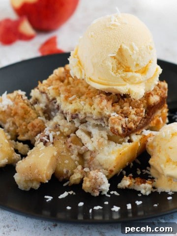 Apple crumble tart, topped with ice cream on a black plate