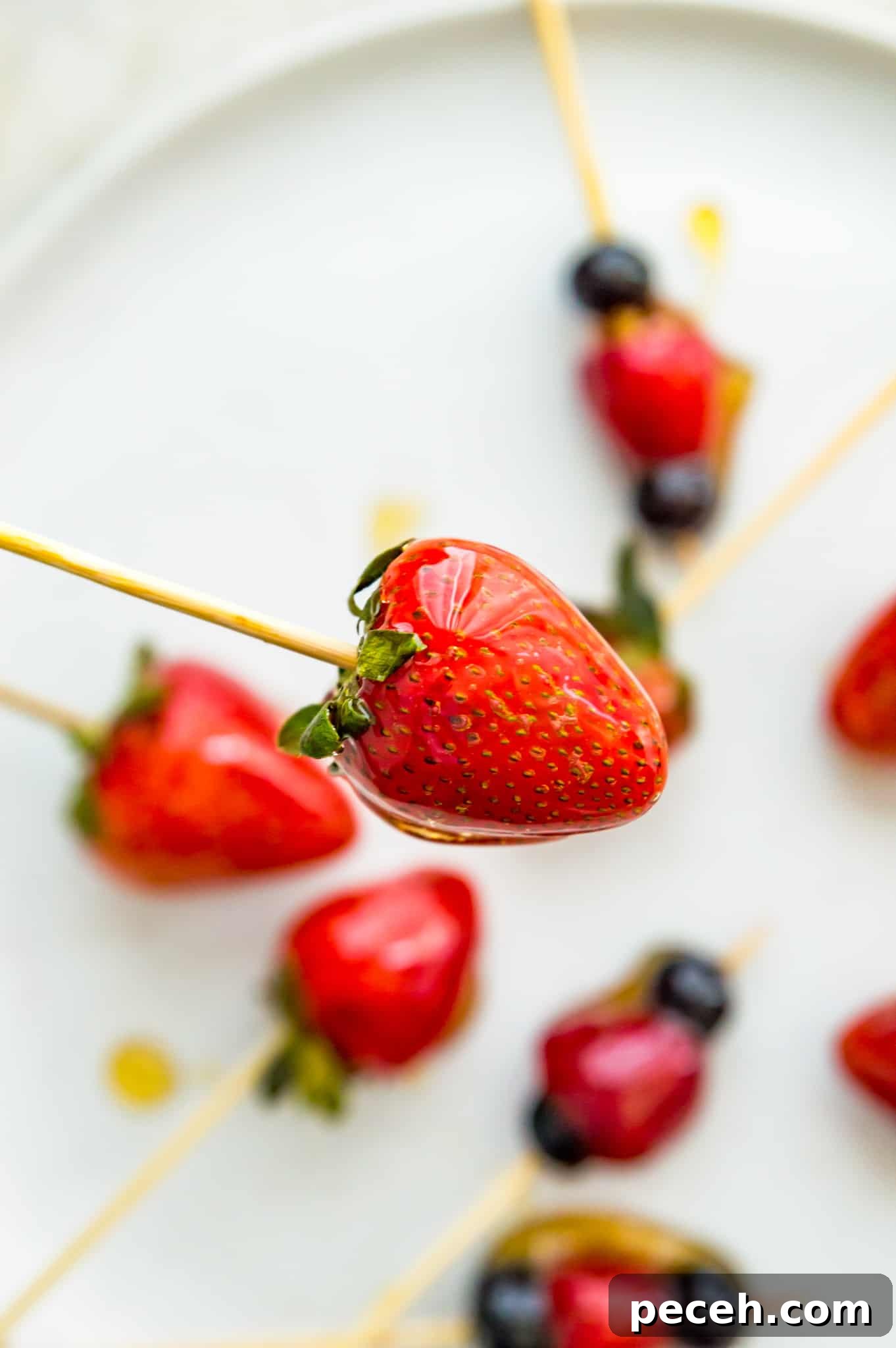 Tanghulu strawberry on bamboo skewer A Tanghulu strawberry on a bamboo skewer with a plate filled with candied strawberries below it.