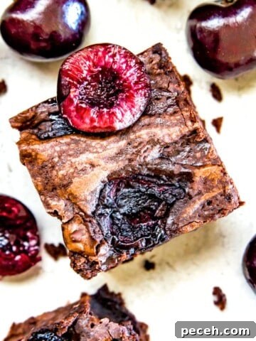 A cherry brownie topped with a fresh cherry cut in half.