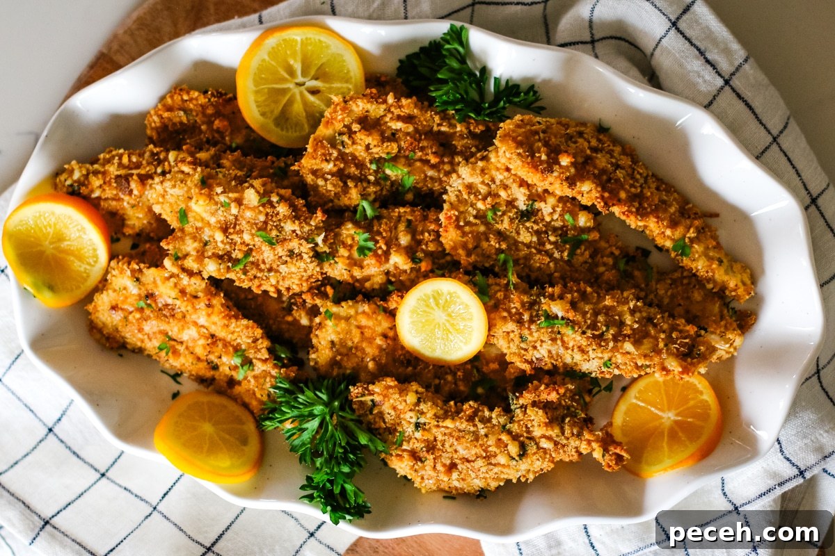 crispy oven-baked chicken cutlets on a plate with lemon slices and fresh parsley.