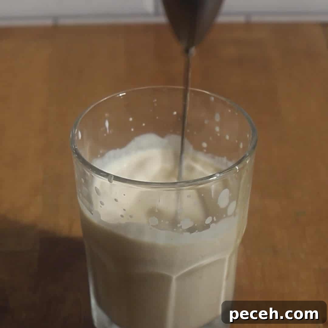 Hand frothing cream and pumpkin mixture in a glass with a handheld frother to make pumpkin cold foam.