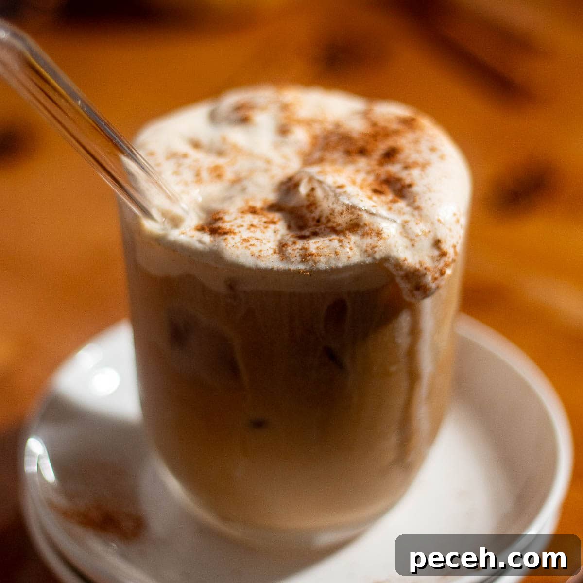 Glass of iced coffee with whipped pumpkin cold foam and a straw, sprinkled with pumpkin spice.