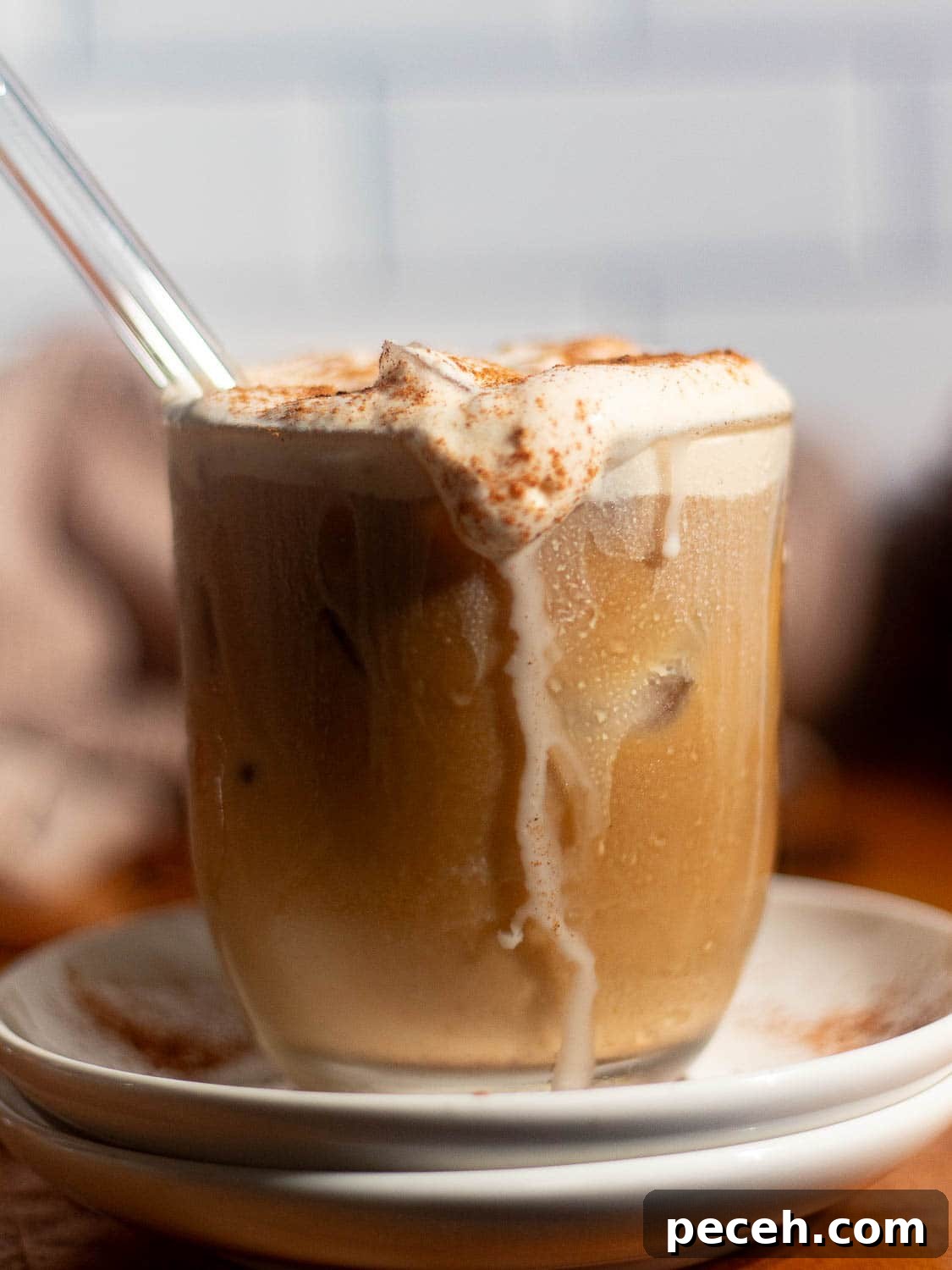 Glass of iced coffee with whipped pumpkin cold foam and a straw, sprinkled with pumpkin spice.
