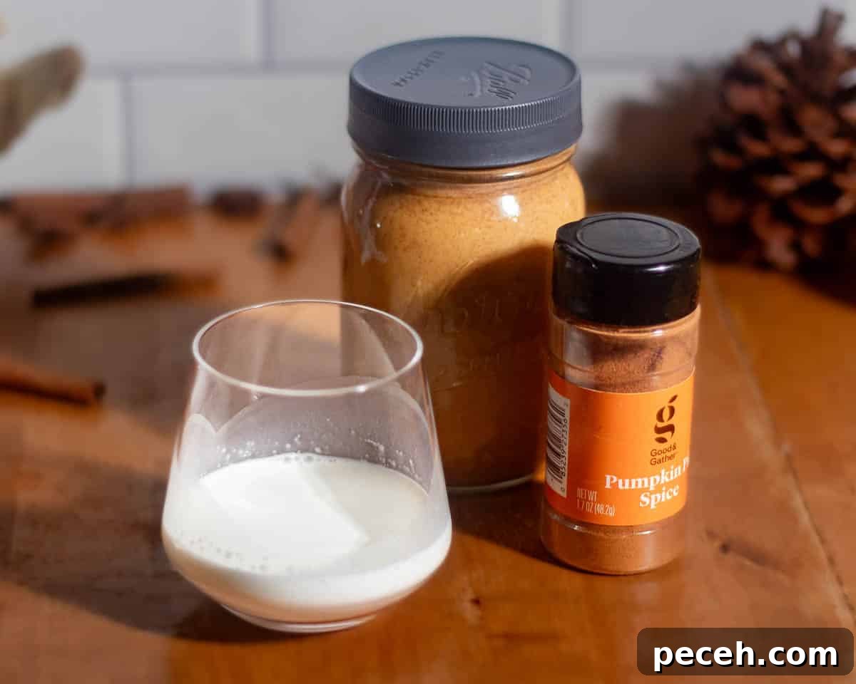 Ingredients for pumpkin cold foam recipe on a wooden table including pumpkin sauce in a mason jar, pumpkin pie spice, and half-and-half in a glass.
