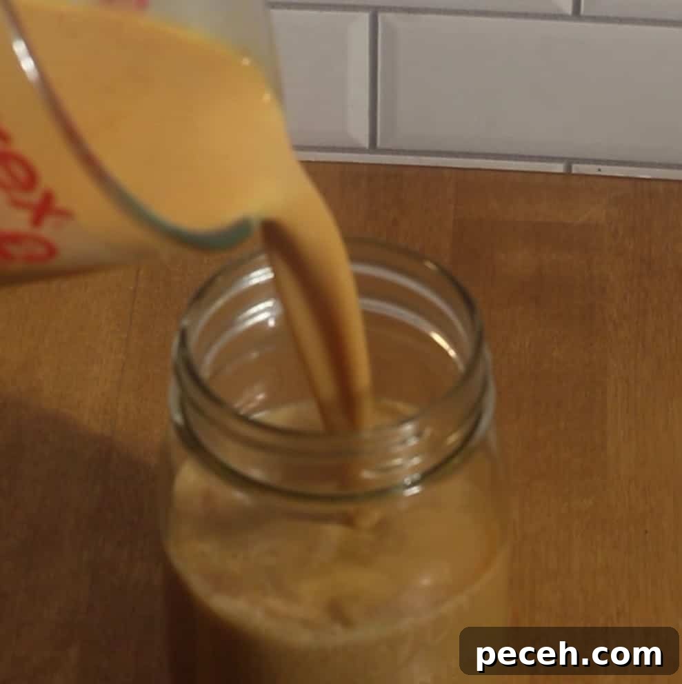 Pumpkin syrup mixture being poured into a mason jar for homemade pumpkin cold foam.