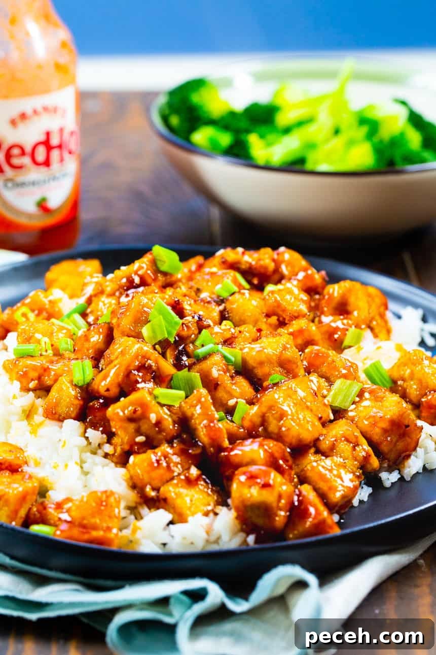 Firecracker Tofu on a plate with broccoli and hot sauce in background.