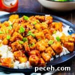 Tofu over rice on a black plate.
