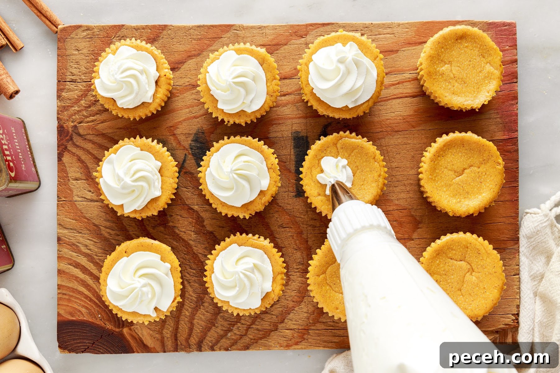 Piping swirls of whipped cream on tops of the mini pumpkin cheesecakes on a cutting board.