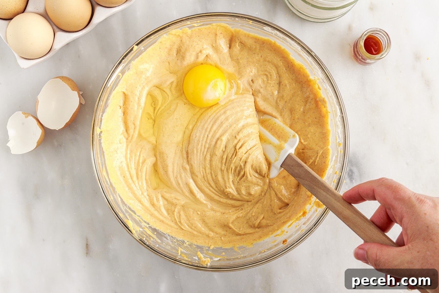 Mixing an egg into mini pumpkin cheesecakes batter using a spatula.