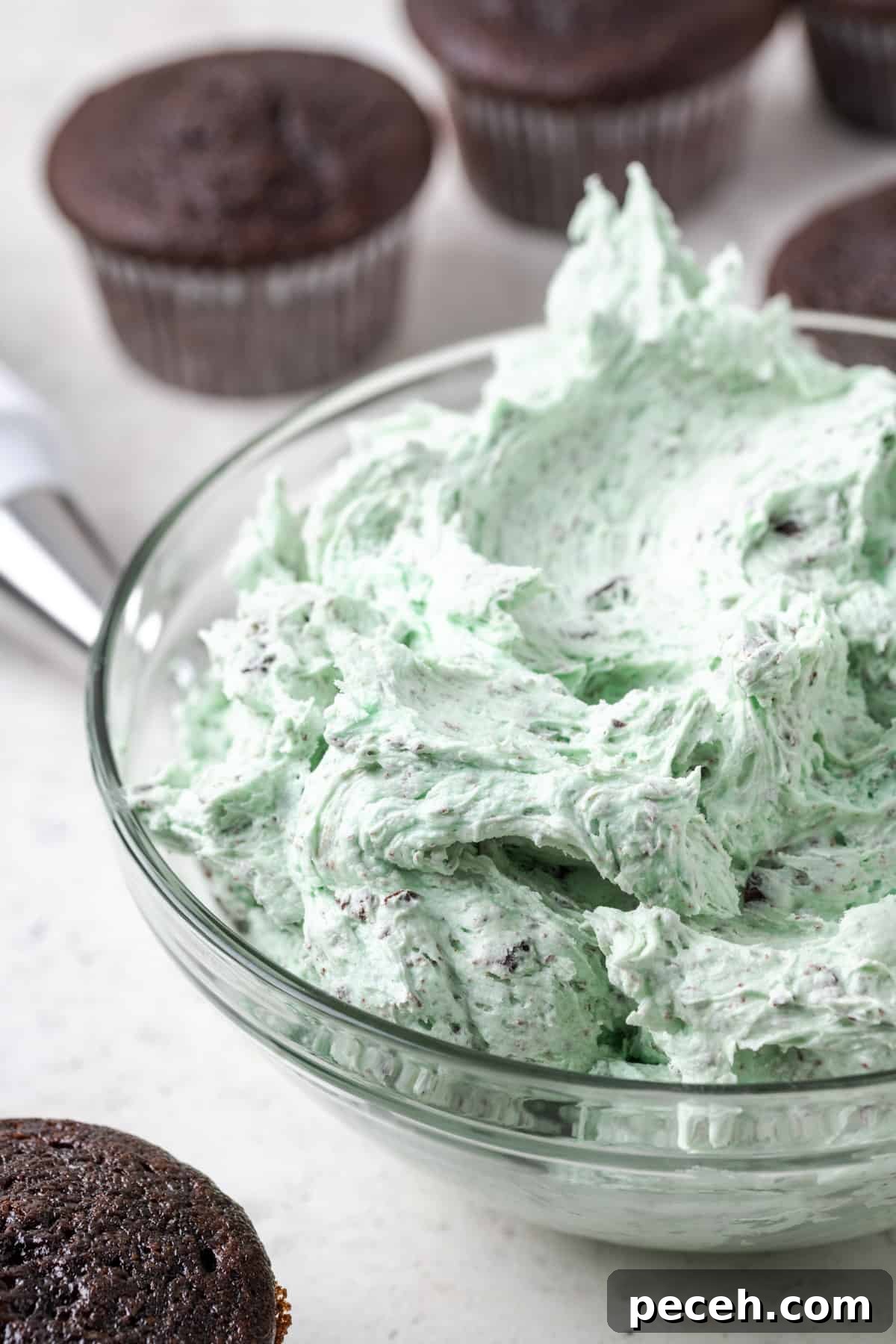 Mint Chocolate Chip Frosting Recipe for Smooth, Creamy Results 2 A bowl of mint chocolate chip buttercream frosting sitting beside some plain chocolate cupcakes.