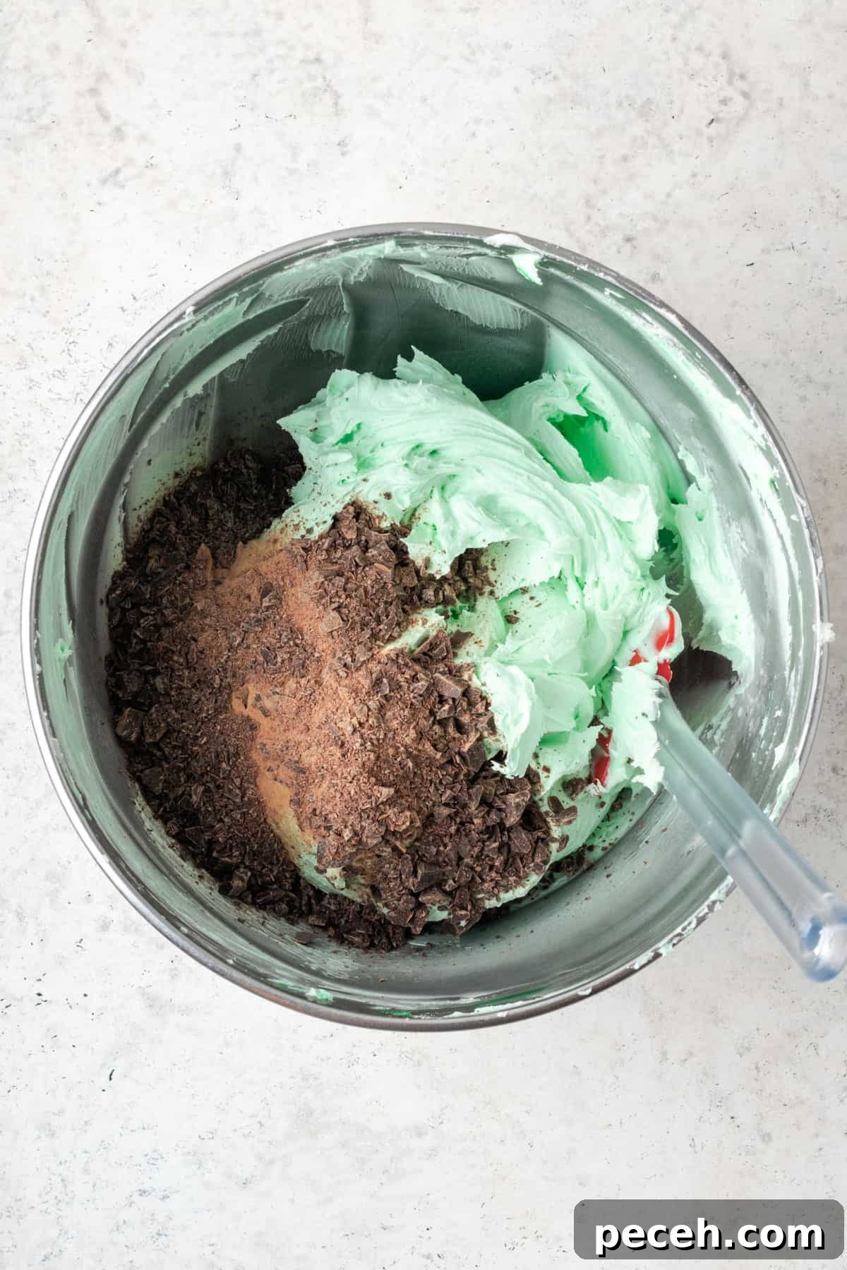 Mint Chocolate Chip Frosting Recipe for Smooth, Creamy Results 8 Chopped chocolate being stirred into the green buttercream frosting with a spatula.