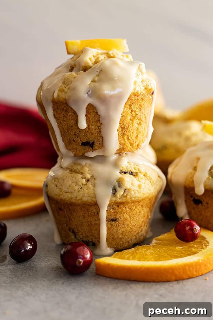 Cranberry Orange Muffins with Zesty Citrus Glaze 2 Two muffins stacked with a glaze dripping down the sides. Cranberries and oranges slices off the sides.